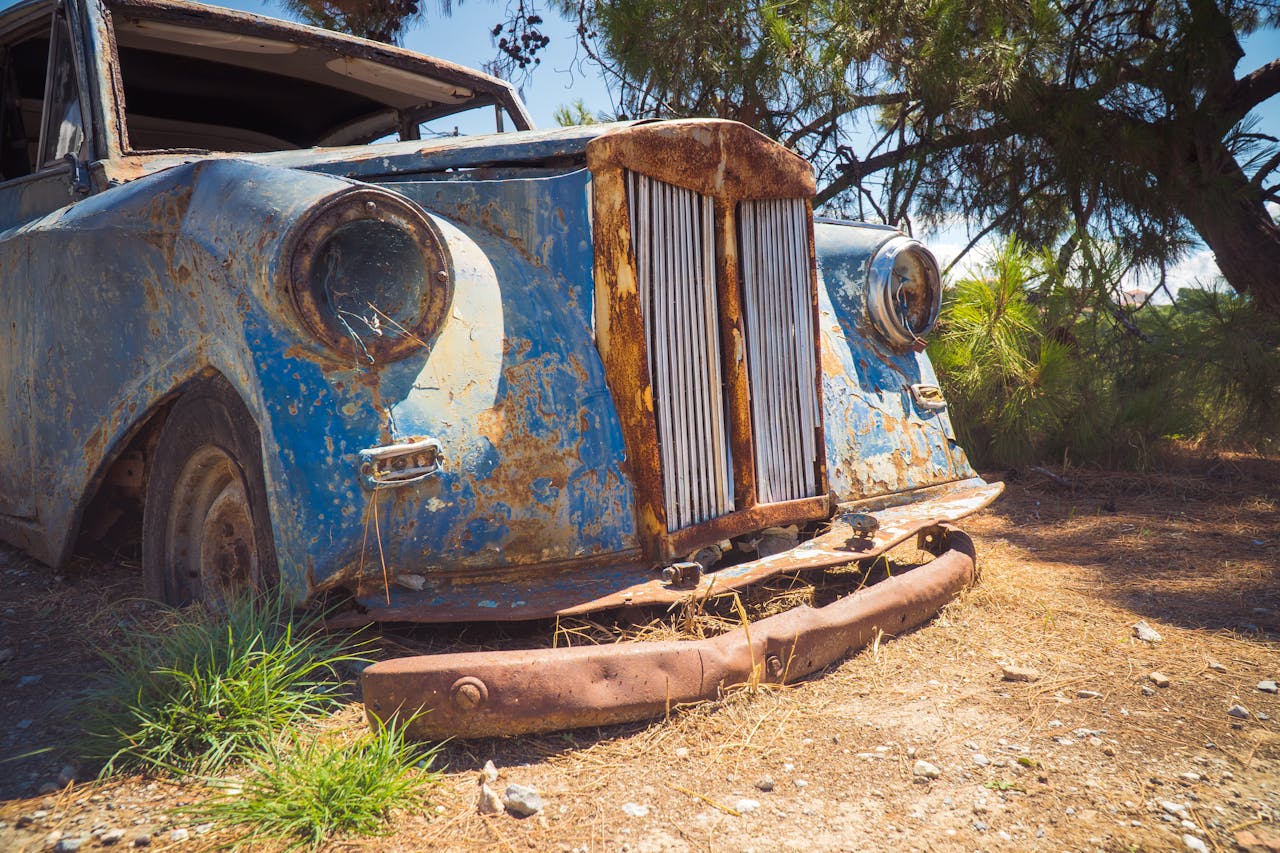 A forgotten vintage car rusts away outdoors, showcasing its decay and history.