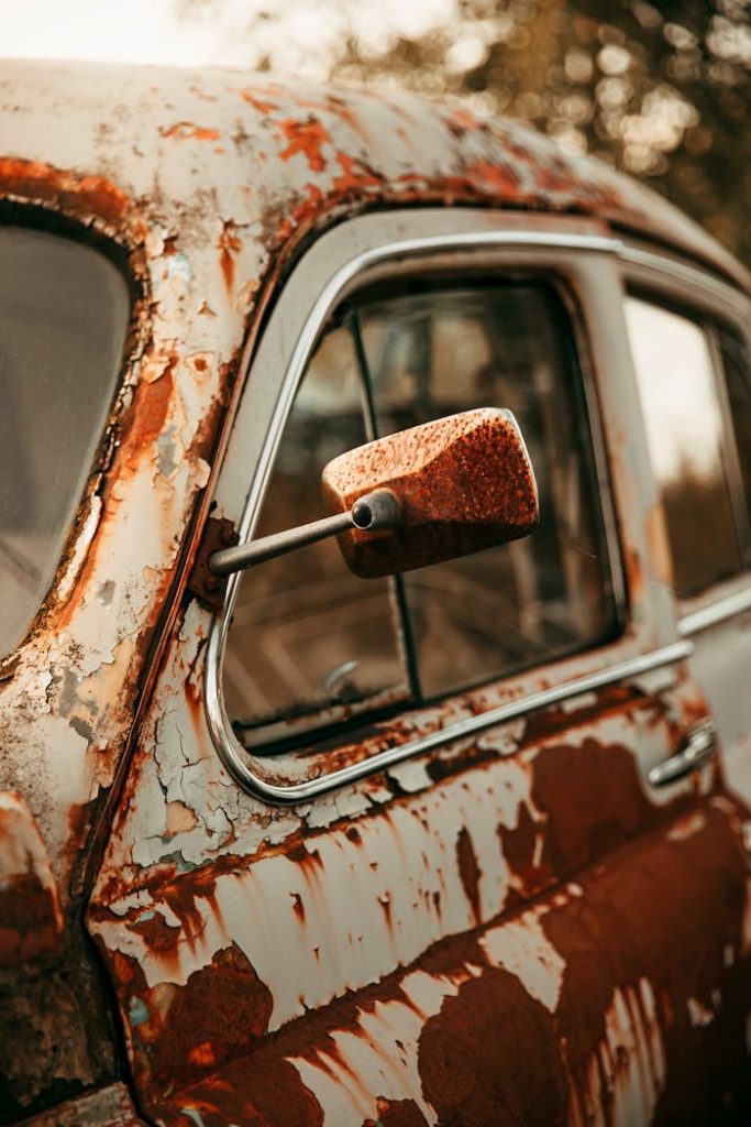 Detailed shot of a rusty vintage car focusing on the side mirror with peeling paint.