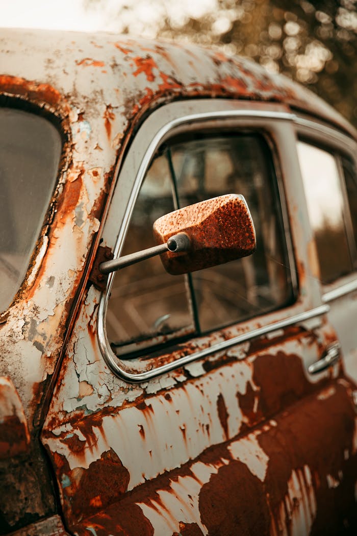 Detailed shot of a rusty vintage car focusing on the side mirror with peeling paint.
